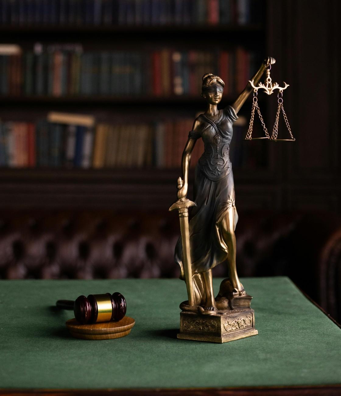 Bronze statue of Lady Justice with scales and sword beside a gavel in a law library
